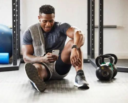 muscular young man using a cellphone while exercising in a gym