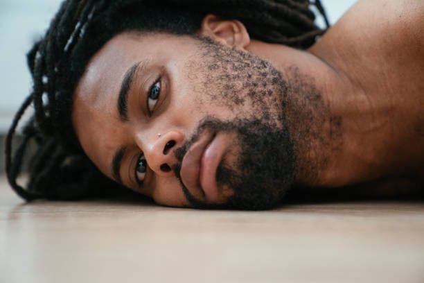 Man with a patchy beard lying face down on the floor.