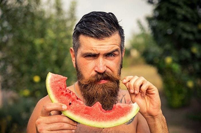 A bearded man holding a watermelon in his hands, showcasing a refreshing summer fruit.